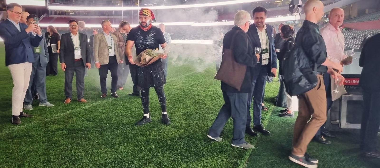 Petiola Wilson conducting a smoking ceremony on the ground at a stadium event as guests gather